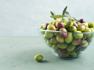 Freshly picked raw green olives in glass bowl on textured background.
