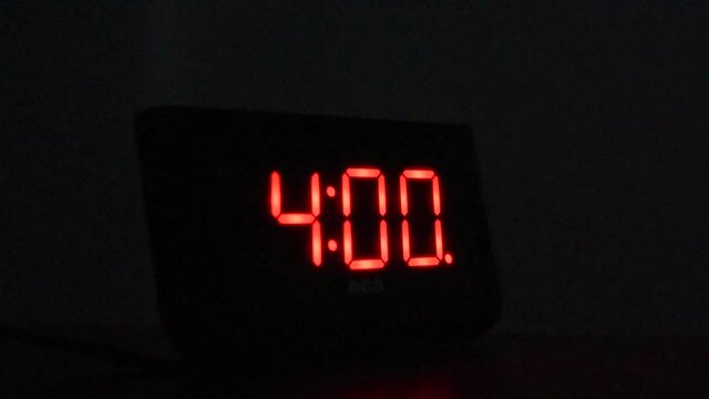Alarm clock going off at 4:00 AM in dark room. Hand reaches out and stops alarm.