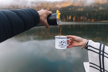 Traveler man pouring a hot drink from thermos to mug. Young woman drinking hot drink at cup. Autumn season.Outdoor Couple,Travel concept.