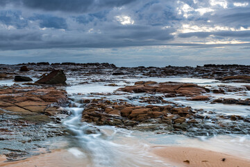 Rock platform, cascades and splashes with rain clouds by the seaside