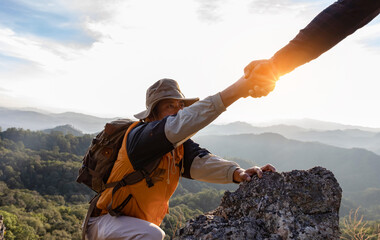 Two Male hikers climbing up mountain cliff and one of them giving helping hand. People helping and,...