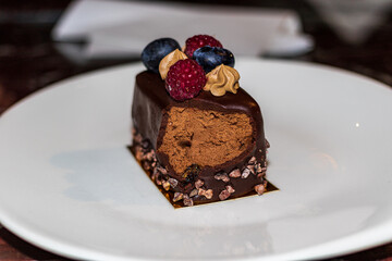 A slice of delicious cake on a white plate. The cake is decorated with fresh berries and dark chocolate. Close-up.