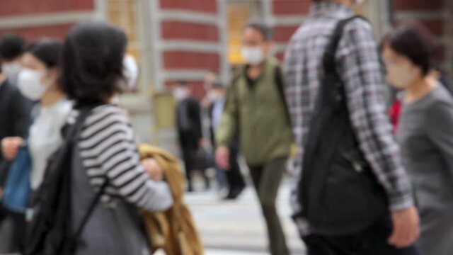 意図的にピントをぼかした東京駅前の横断歩道を渡るマスク姿のビジネスマンたちのスローモーション動画
