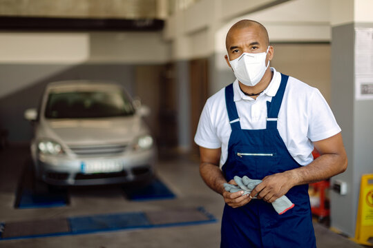 African American auto mechanic wearing protective face mask in a workshop during coronavirus pandemic.