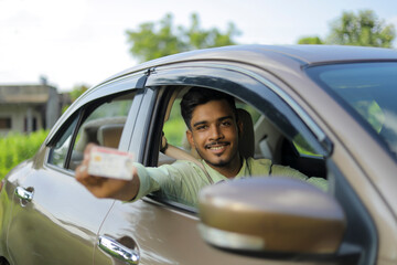 Young indian businessman or employee sitting in car and showing card