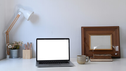 Creative designer workspace with white blank screen computer laptop and equipment on white desk.