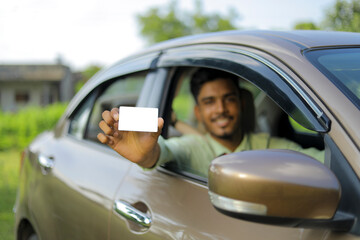 Young indian businessman or employee sitting in car and showing card