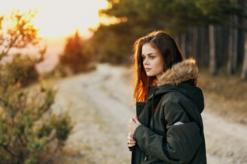 woman in jacket outdoors on background of sun trees lifestyle