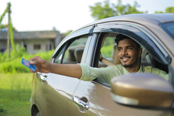 Young indian businessman or employee sitting in car and giving card