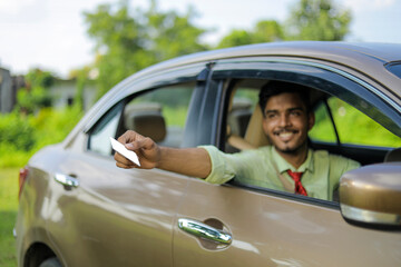 Young indian businessman or employee sitting in car and giving card