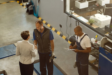 Above view of happy mechanic greeting a businesswoman in a repair shop.