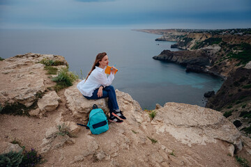Fototapeta na wymiar Attractive woman is sitting on the edge of the mountain with a sea view, reading a book.
