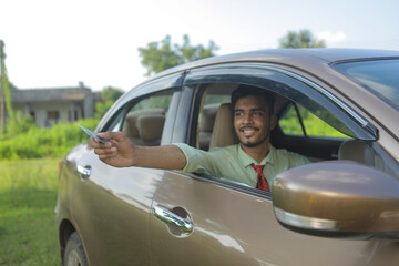 Young indian businessman or employee sitting in car and giving card