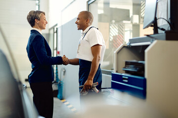 Obraz premium Happy businesswoman handshaking with African American mechanic at auto repair shop.