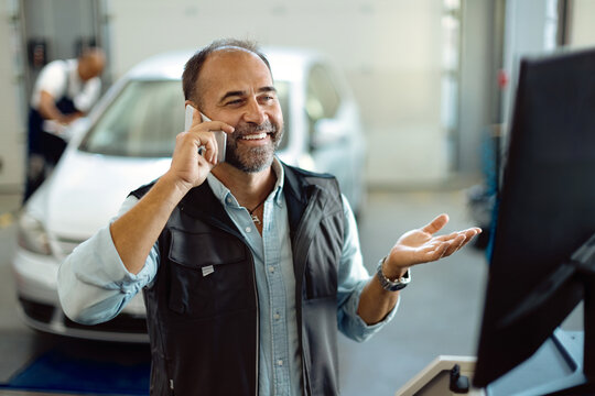 Happy mechanic making a phone call while working at auto repair shop.