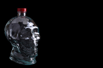 Empty glass bottle in the form of a skull on a black background with copy space