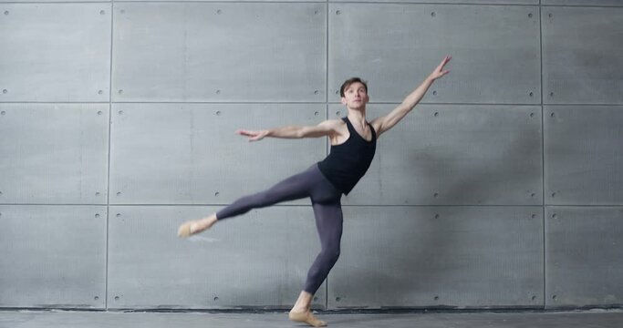 Elegant male, ballet dancer performs acrobatic elements of a ballet dance on a gray background, 4k slow motion.