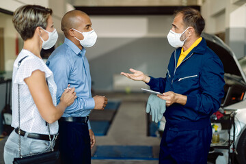 Obraz premium Auto mechanic and a couple wearing face masks while talking at car service workshop.
