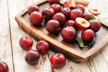 Board with fresh ripe plums on wooden table