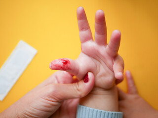 Drop of red blood from kid finger. Mom holds the kid wounded hand. Cut help concept