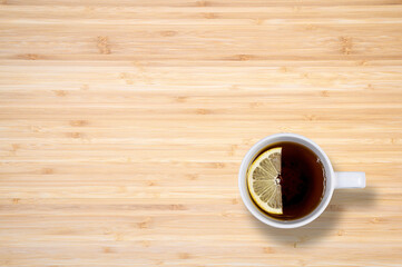 A cup of black tea with lemon on a wooden table. View from above. There is a free space.