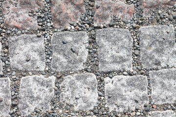 The cobblestone pavement is made of stone in the form of slabs with uneven edges and pebbles between them. Textured background.