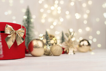 Fototapeta na wymiar Red Christmas gift box with a gold bow on the background of bokeh, Christmas trees and toys
