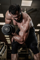 strong bearded young male training biceps muscle using heavy dumbbell in sport gym