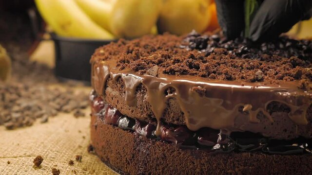 Chocolate cake on a straw-covered table. The chef puts the final touch. Close up. Background enriched with chocolate chips and fruits.