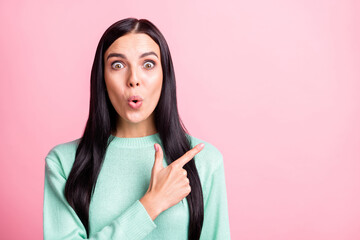 Photo portrait of shocked girl pointing finger at blank space isolated on pastel pink colored...