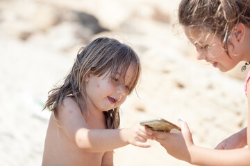  Family beach day.Sisters looking at photos taken with mobile on the beach