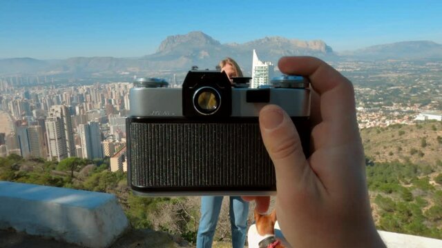 Interesting video concept of creative content creator make photos of happy tourist smiling young woman on top of travel spot though viewfinder of vintage film analog camera. POV travel blogger concept