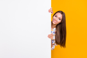 Photo portrait of funny girl hiding behind white wall with blank space isolated on vivid yellow...