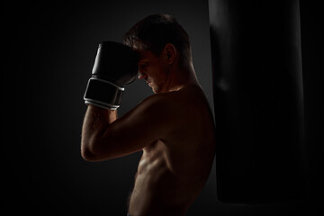 Fototapeta na wymiar handsome fit male boxer in black gloves standing near punching bag on dark background