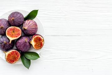 Fresh whole and sliced figs on a plate with green leaves. Top view