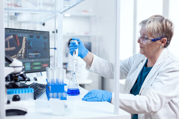 Senior scientist woman taking sample from glass flask using molecular pipette. People in innovative...