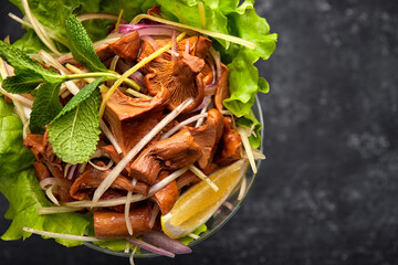 Pickled chanterelle mushrooms, with herbs and lettuce, in a glass bowl, on a black background