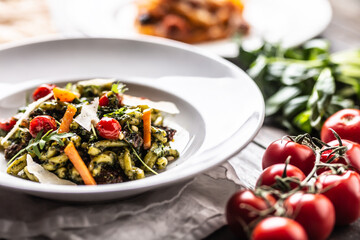 Pasta with green pesto, cherry tomatoes, parmesan cheese and olive oil in a plate