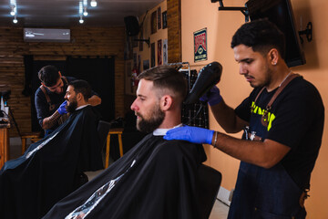 Barber drying his client's hair with a hair dryer - Young men barbers working in their barbershop.