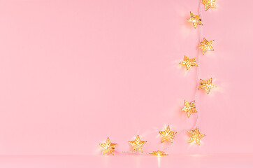 Festive golden stars glowing lights on soft light pink background, copy space.