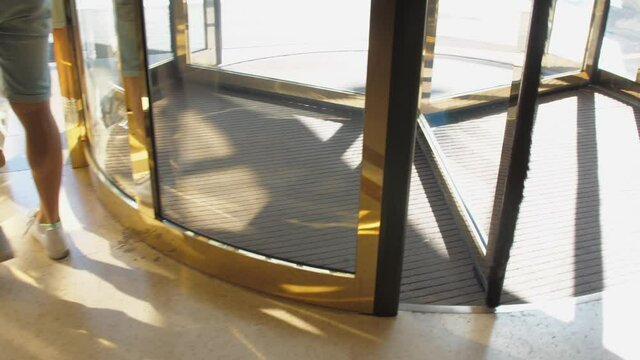 Men legs in white snickers walk along hotel lobby past golden revolving door on sunny day close view slow motion. Concept visiting hotel