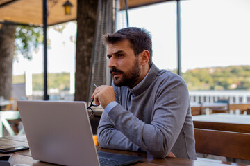 Portrait of a young businessman working outside on the laptop with glasses in hand.