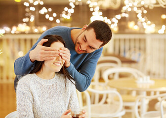 people, surprise and dating concept - happy couple drinking tea at cafe or restaurant over festive lights