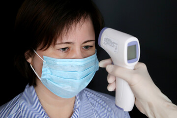 Coronavirus symptoms, doctor measures body temperature of woman in medical mask. Digital infrared...