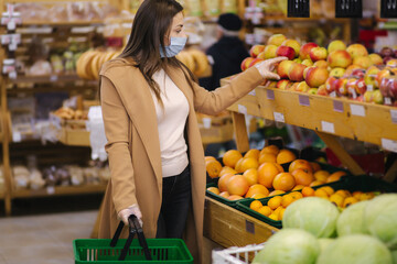 Female buyer wearing a protective mask and gloves in supermarket. Shopping during the pandemic quarantine. Woman buying fresh fruits