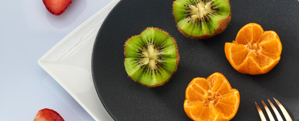 Fresh kiwi fruit and tangerines are on a black plate.Light background