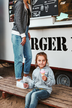 Little Girl Eating Ice Cream Sitting On A Step At Front Of Food Truck During Family Time On Summer Vacations