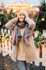 Portrait of Young woman walking in Christmas market decorated with holiday lights in the evening. Feeling happy in big city. Spending winter vacations in Red square, Moscow, Russia.