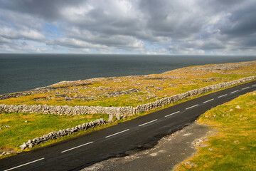 Small narrow asphalt road by the Atlantic ocean. Burren area, West coast of Ireland. Warm sunny day. Cloudy sky