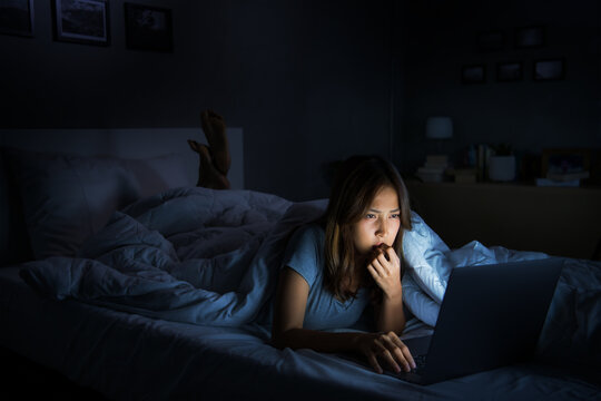 Young woman having sore and tired eyes when using laptop while lying in bed at night